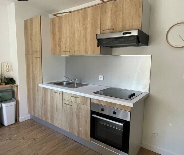 Una cocina moderna con armarios de madera clara, un lavamanos de acero inoxidable y un horno empotrado.