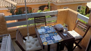 A balcony with a table set for two, a chair, a hanging chair, and a view of neighboring buildings. - Veramarinas apartment - relax and privacy (AN)