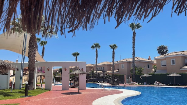 A pool area with a curved edge, palm trees, and a covered walkway. - Veramarinas apartment - relax and privacy (AN)