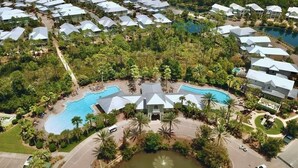 An aerial view of a resort with multiple buildings, a central swimming pool, and surrounding greenery.