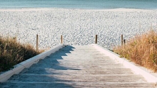 A wooden boardwalk leading to a sandy beach with the ocean in the background.