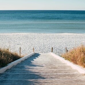 A wooden boardwalk leading to a sandy beach with the ocean in the background.
