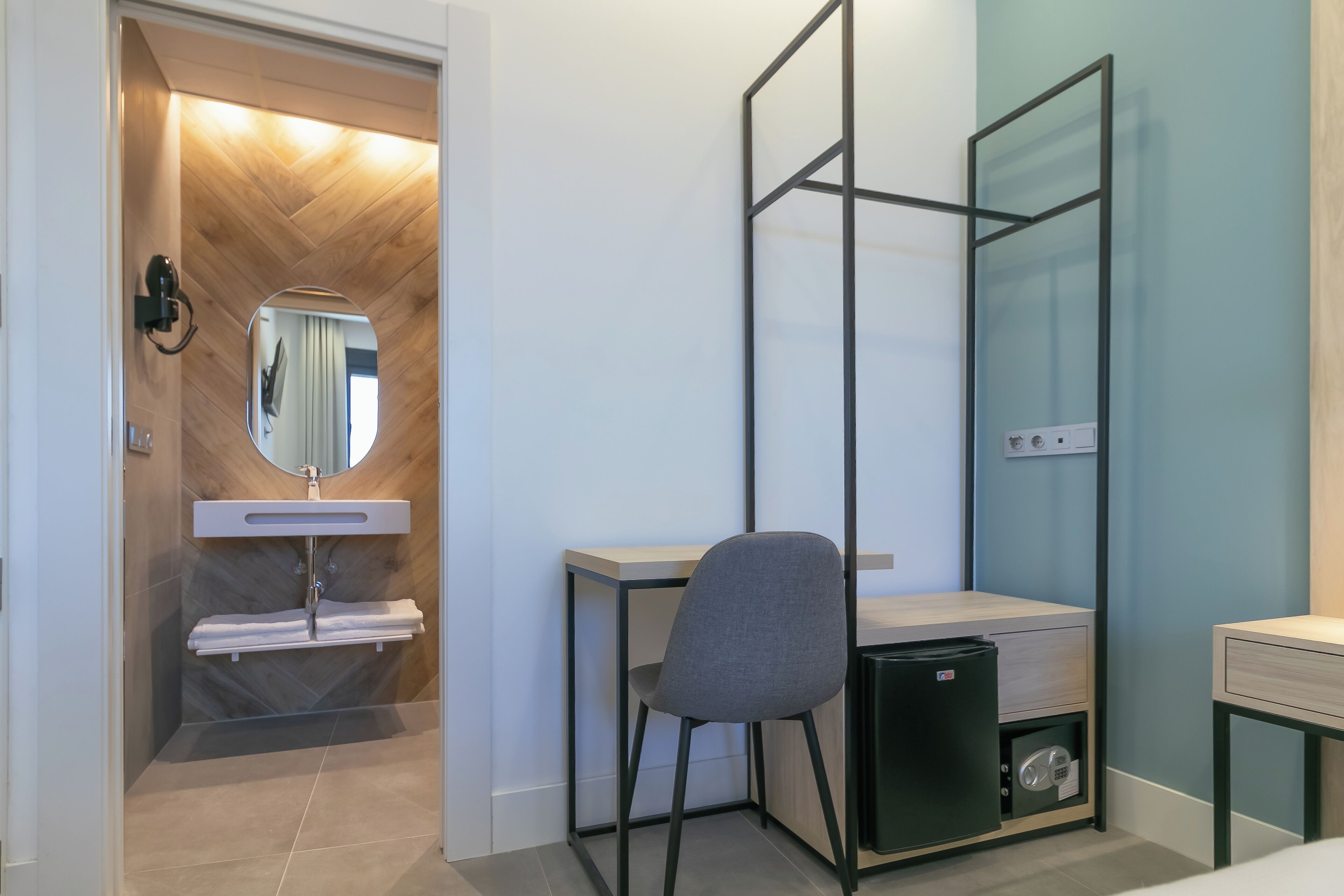 Un baño moderno con tocador de madera, un espejo, toallero y un cubo de basura pequeño.