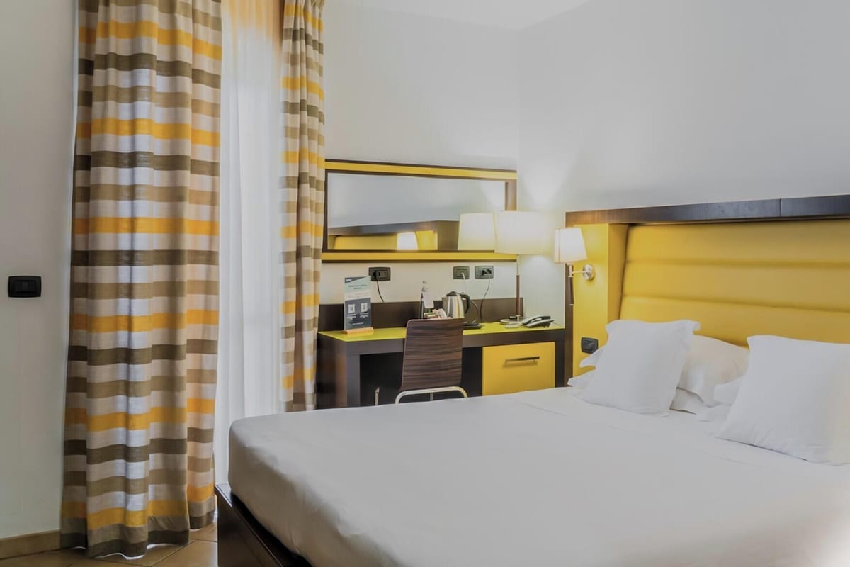 A hotel room with a bed, a desk, a chair, and a mirror.