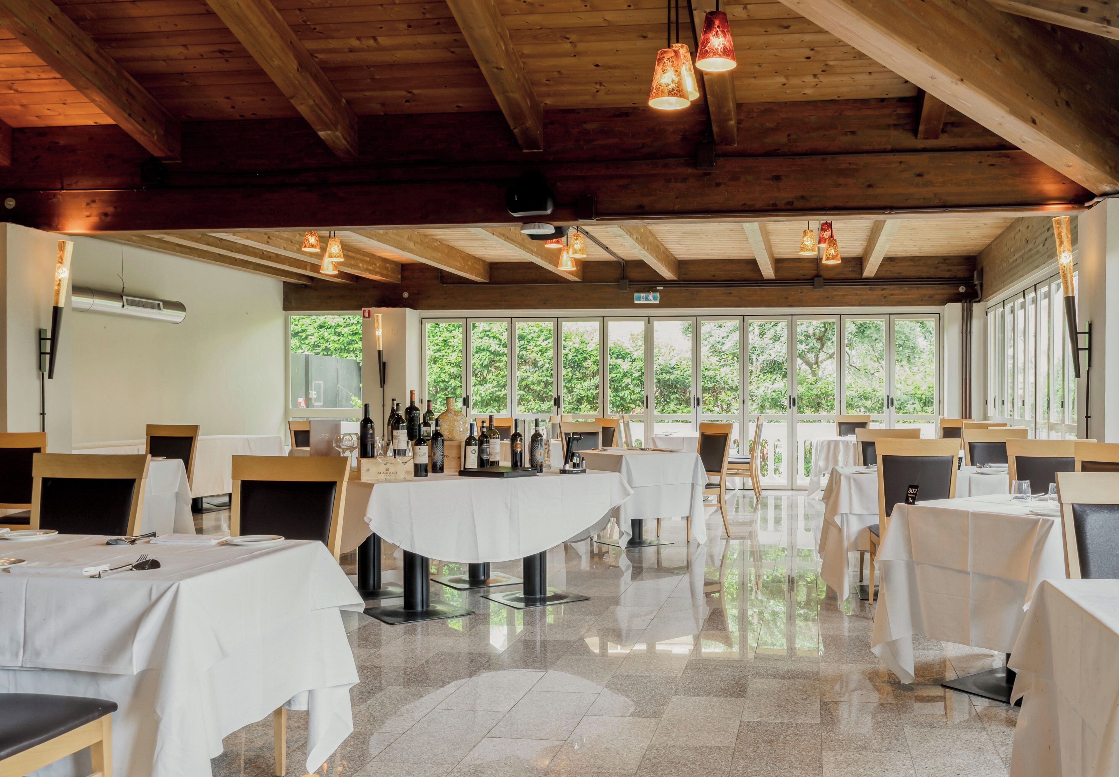 Restaurante com vigas de madeira, grandes janelas e mesas preparadas para refeições.