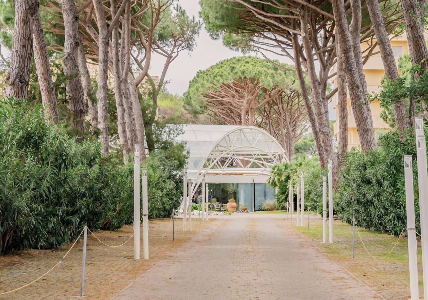 A pathway leading to a covered structure with a glass roof, surrounded by trees and greenery.