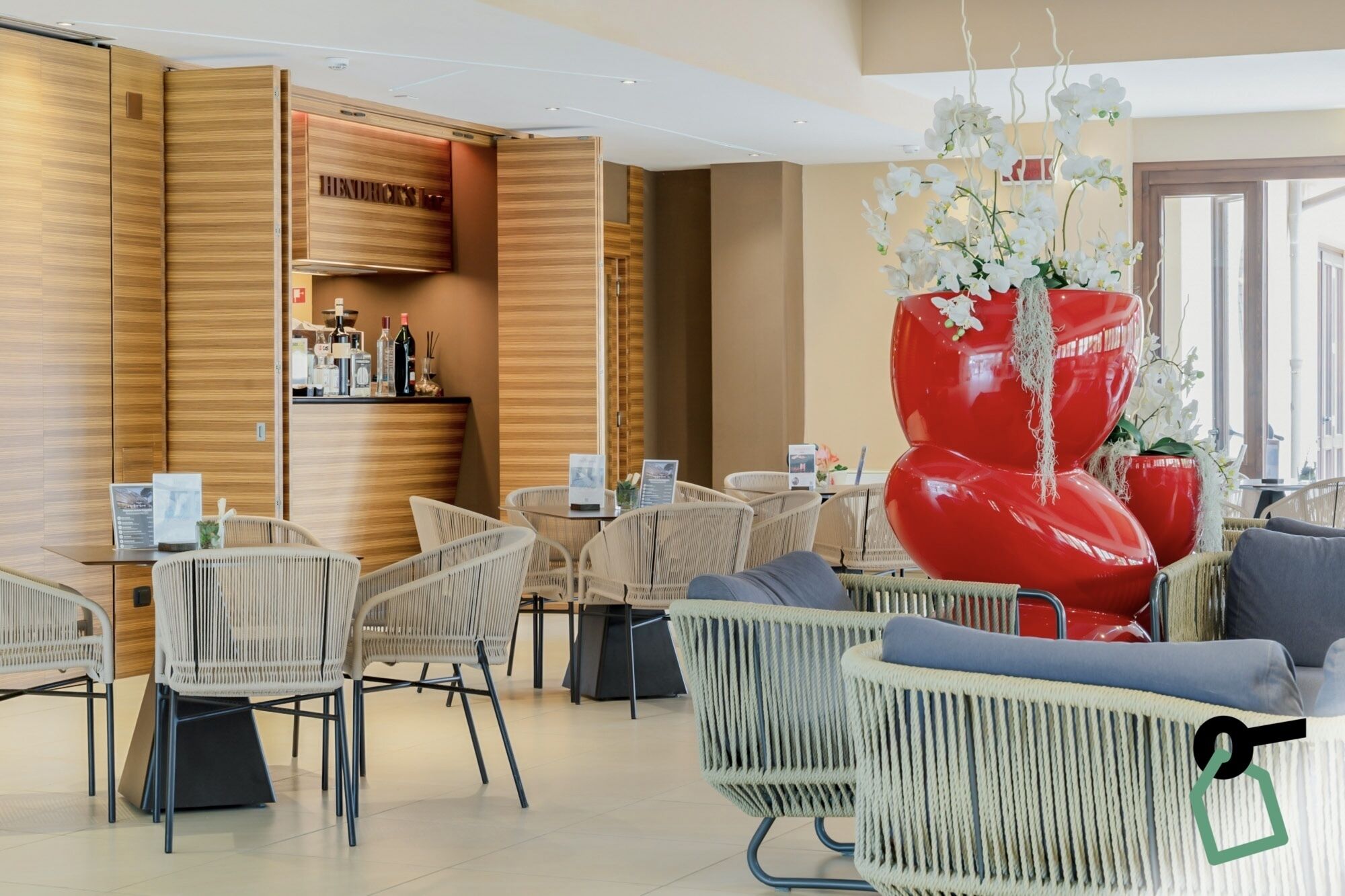 A modern hotel lobby with wicker furniture, a bar area, and a unique red sculpture.