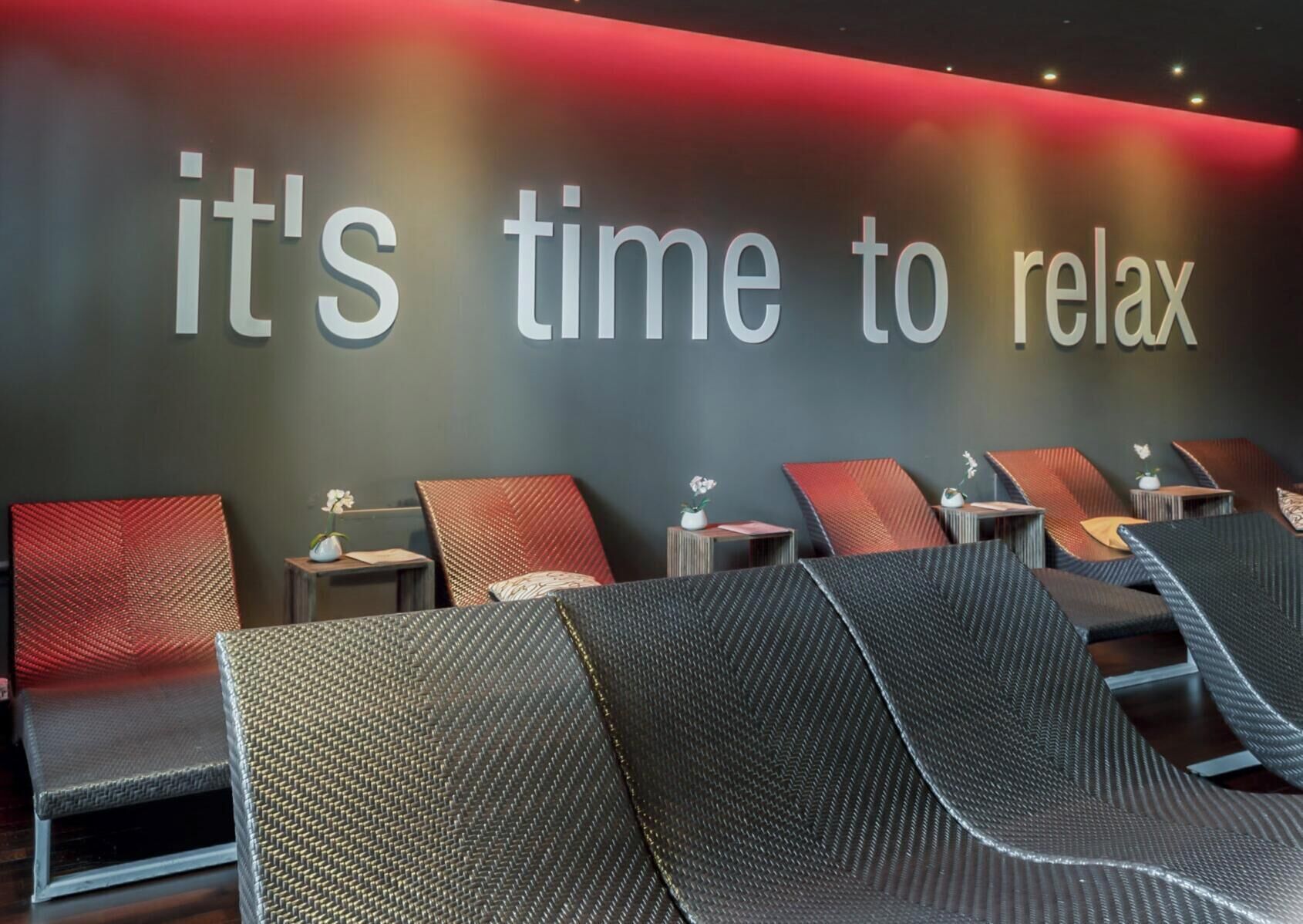 Espaço relaxante com um letreiro na parede que diz 'é hora de relaxar' e várias poltronas.