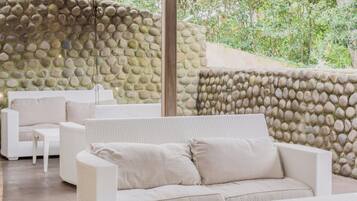 A covered outdoor seating area with a stone wall, white wicker furniture, and a red umbrella.