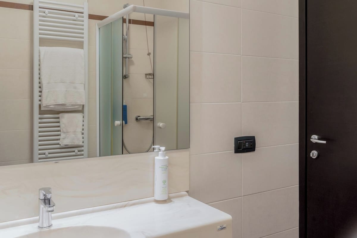 A bathroom with a sink, mirror, towel rack, shower, and a door.