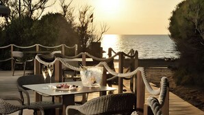 A seaside dining area with wicker chairs and tables, a rope barrier, and a view of the ocean at sunset. - Hotiday Marina di Bibbona (Marina di Bibbona)