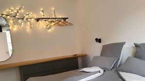 A modern bedroom with a bed, grey bedding, a bedside table, a mirror, and string lights on the wall. - Alpaca Lodge Kirchwahlingen (Kirchwahlingen)