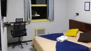 A hotel room with a bed, a desk with a chair, a television, and a window with curtains. - Hotel princesinha do cafe (Vassouras)