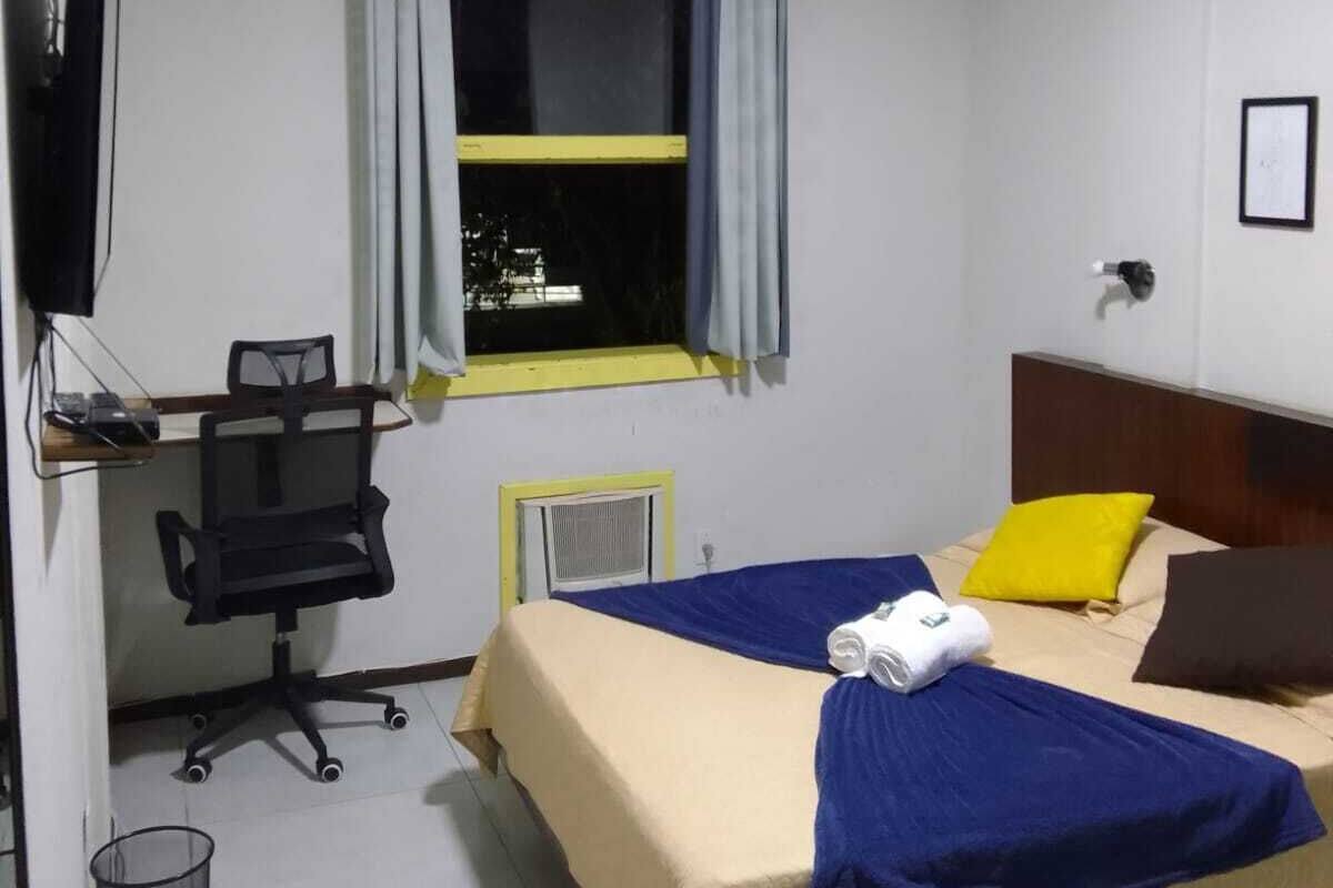 Une chambre d’hôtel comprenant un lit, un bureau avec une chaise, une télévision et une fenêtre avec des rideaux.