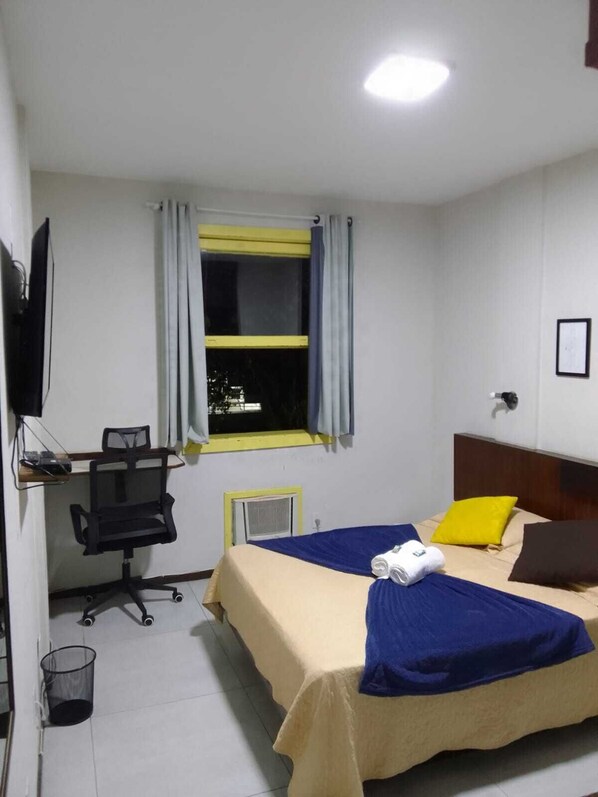 A hotel room with a bed, a desk with a chair, a television, and a window with curtains. - Hotel princesinha do cafe (Vassouras)