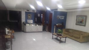A spacious lobby with a reception desk, a sofa, and a coffee table. - Hotel princesinha do cafe (Vassouras)