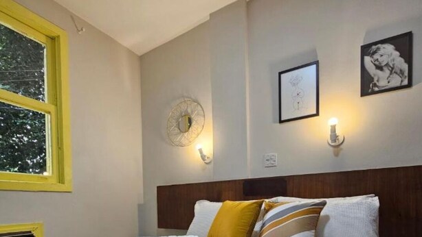 A neatly made bed with white linens and rolled towels, a wooden headboard, and wall-mounted light fixtures. - Hotel princesinha do cafe (Vassouras)