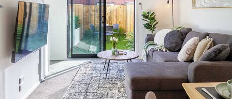 Una sala de estar moderna con un sofá gris, una mesita redonda y un ventanal corredizo que da a un jardín trasero.