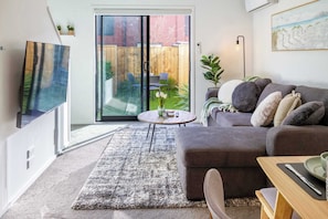 A modern living room with a grey sofa, a small round table, and a sliding glass door leading to a backyard.