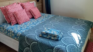 Een kamer met een houten plafond, een bed met beddengoed met een patroon, een hanglamp en een raam met gordijnen.