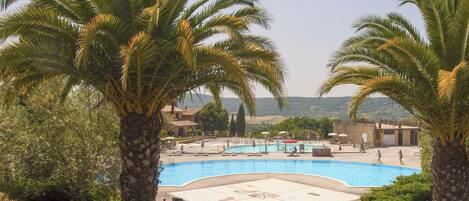 A swimming pool with a surrounding deck, palm trees, and a view of distant hills.