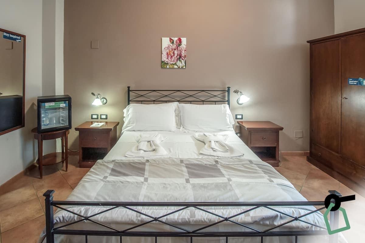 A neatly made bed with a checkered bedspread, two bedside tables with lamps, a wall-mounted TV, and a wooden wardrobe.