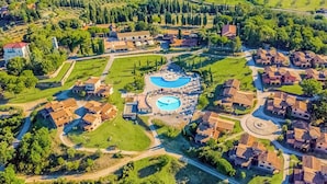 Luftaufnahme eines Resorts mit einem zentralen Schwimmbecken, umgeben von Villen und angelegten Gärten.