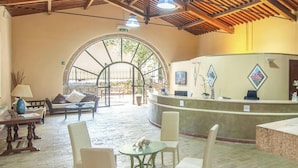 Un espace d’accueil doté d’un plafond en bois, d’un comptoir de réception, d’un coin salon avec des chaises et une table, et offrant une vue à travers une porte en arc de cercle.