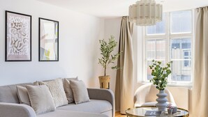 Una sala de estar moderna con un sofá gris, una mesa de centro redonda de vidrio y una lámpara colgante.