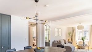 Una sala de estar moderna con comedor, que presenta una mesa de comedor de madera, un sofá gris y una araña.