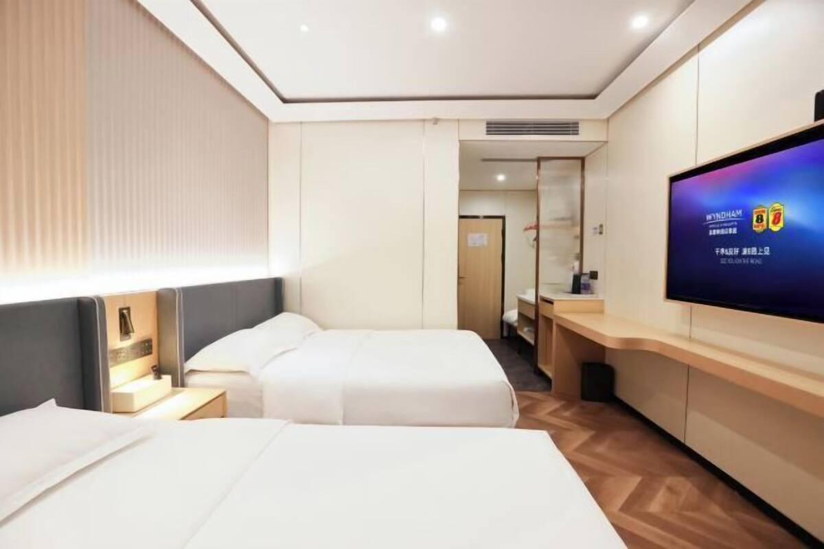 A hotel room with two beds, a TV on the wall, and a wooden floor.