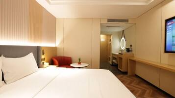 A hotel room with a large bed, a small table, a red chair, a mirror, and a TV.