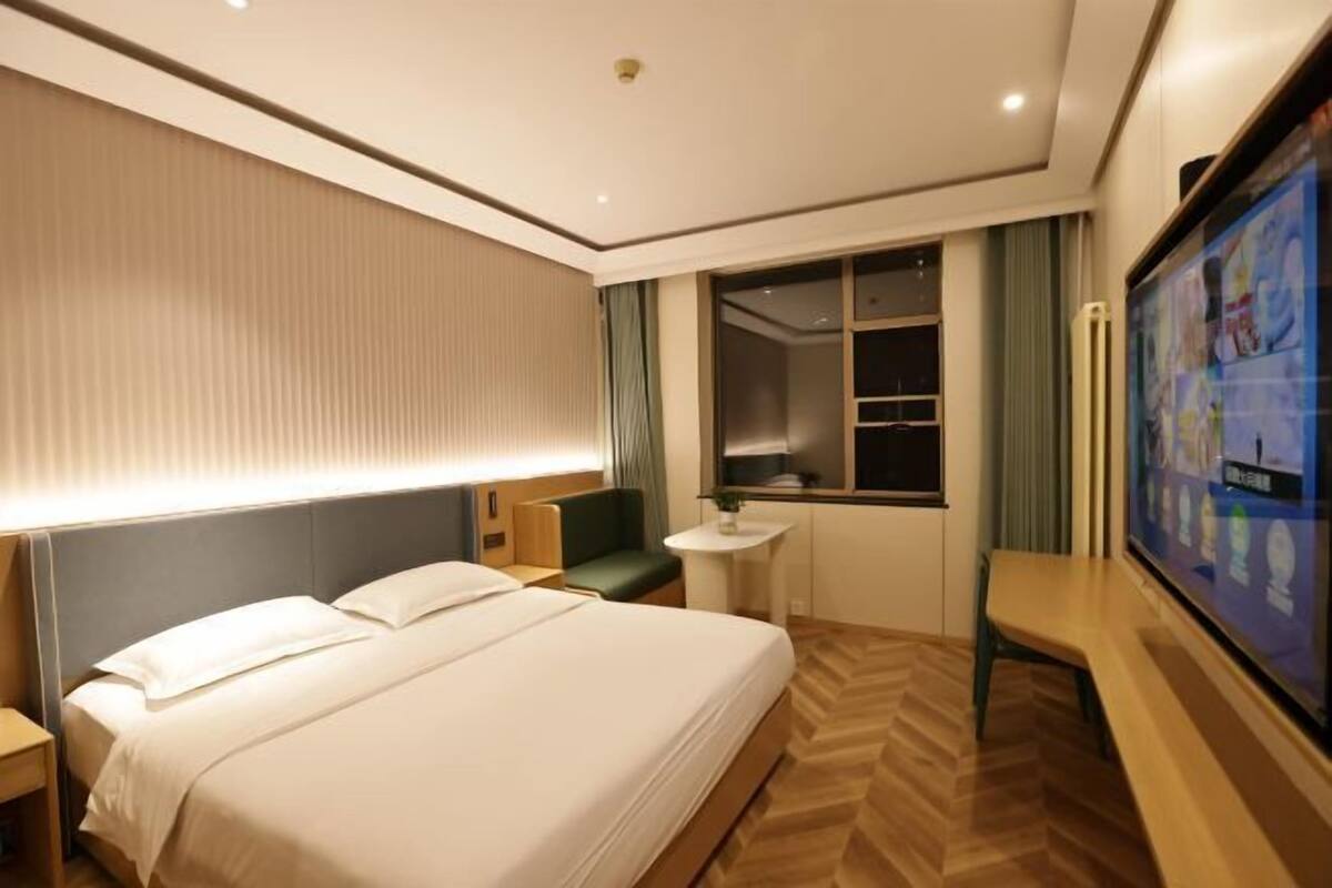 A hotel room with a large bed, a desk, a TV, and a window with curtains.