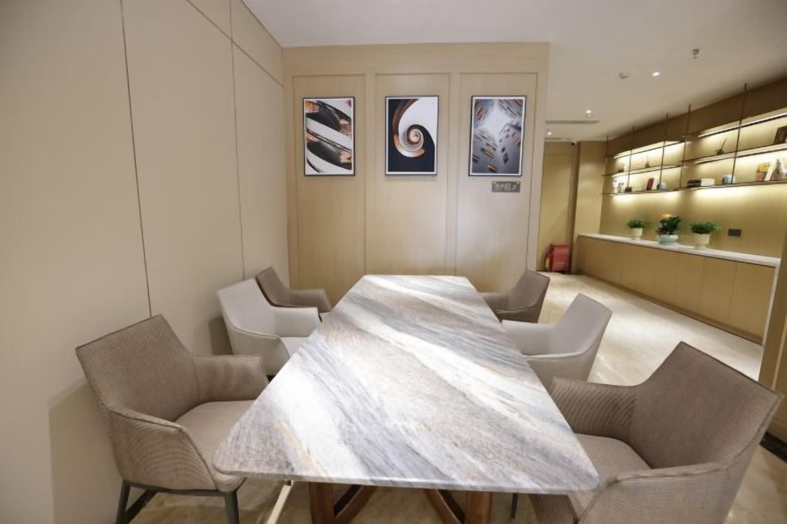 Un salón de conferencias con una mesa de mármol y sillas modernas, una zona de cocina con mostrador y plantas, y obras de arte enmarcadas en la pared.