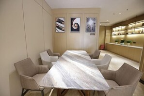 Ein Konferenzraum mit einem Marmortisch und modernen Stühlen, eine Küchenzeile mit Arbeitsplatte und Pflanzen sowie gerahmte Kunstwerke an der Wand.