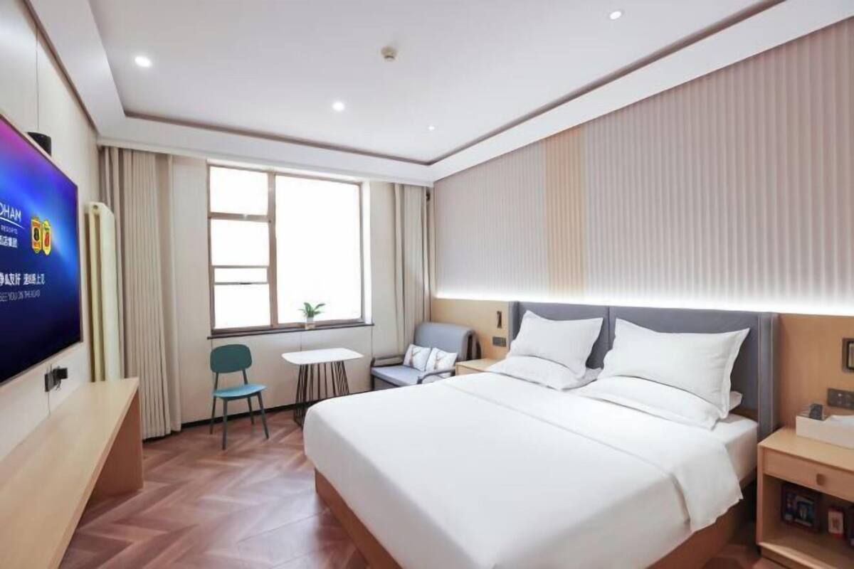 A hotel room with a large bed, a desk, a chair, a small table, and a TV on the wall.