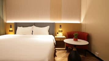 Quarto de hotel com cama grande, mesas de cabeceira, uma pequena mesa redonda com uma planta e uma cadeira vermelha.