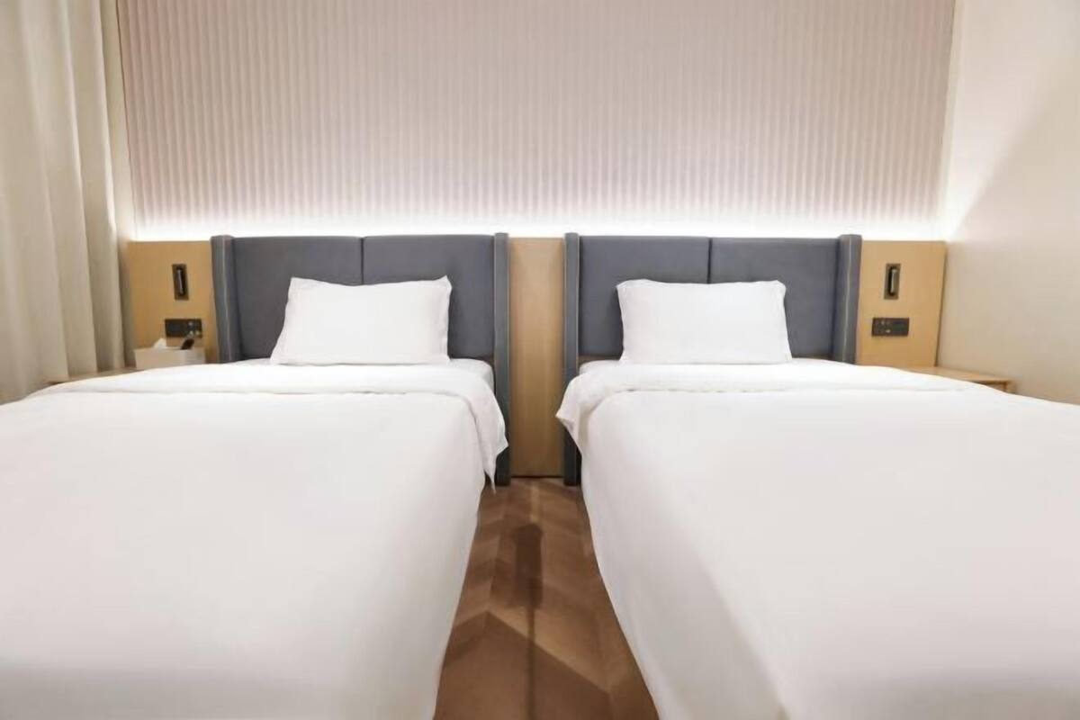 A hotel room with two beds, a wooden floor, and a window with blinds.
