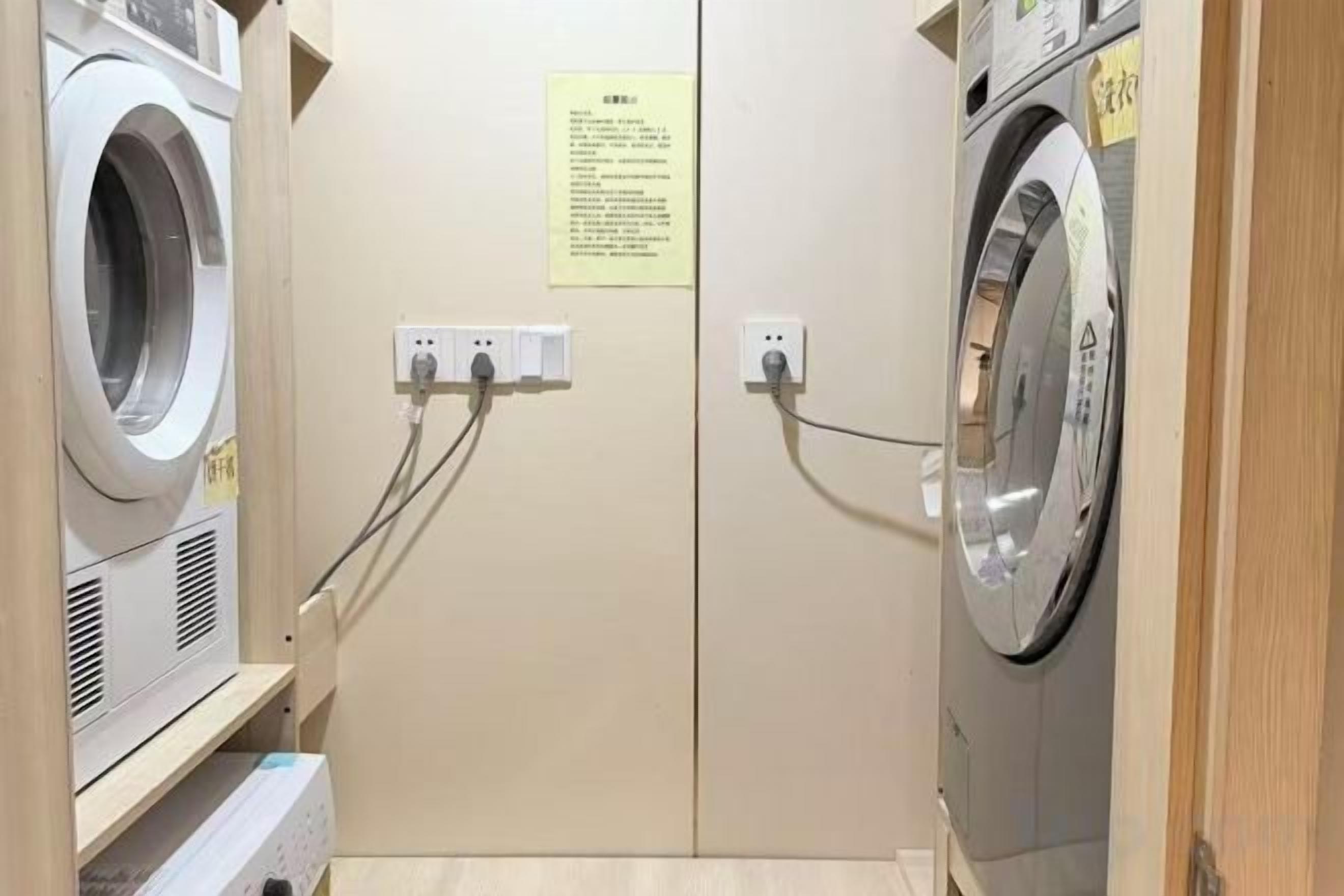 A laundry room with two washing machines, electrical outlets, and a sign on the wall.