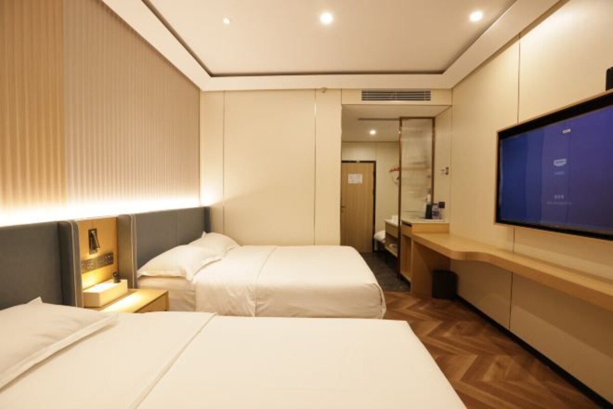 A hotel room with two beds, a TV, a desk, and a bathroom visible through a glass door.