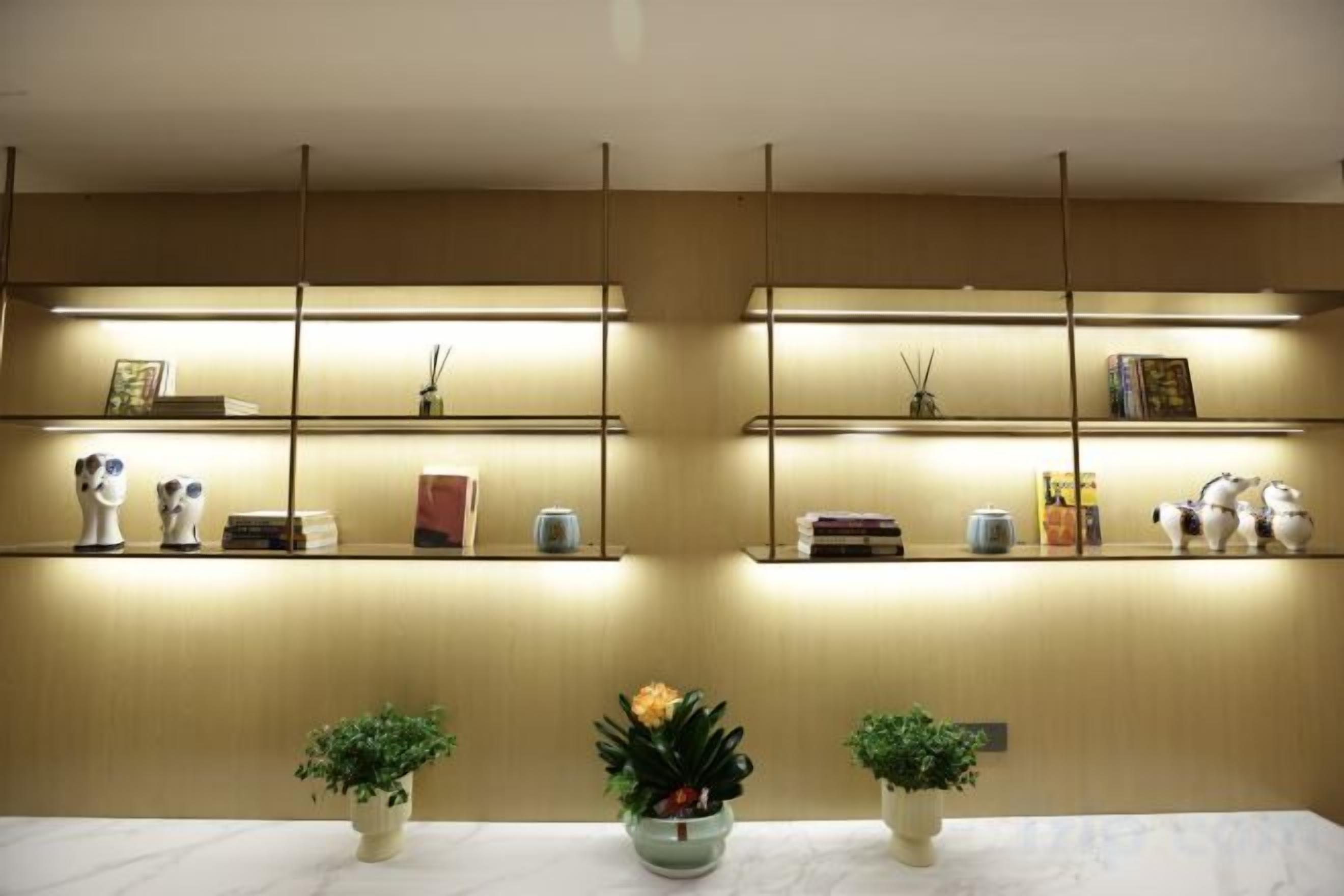 A reception area with a marble table, two potted plants, and shelves with various items.