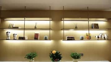 Uma área de recepção com uma mesa de mármore, duas plantas em vasos e prateleiras com diversos objetos.
