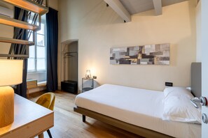 A hotel room with a bed, a desk, a chair, a lamp, a wall art piece, and a window with curtains. - Palazzo Odescalchi by Wonderful Italy - Apt 6 (Como)