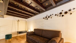 A modern living room with a brown sofa, wooden flooring, a green ottoman, a small round table, and a wall-mounted light fixture. - Palazzo Odescalchi by Wonderful Italy - Apt 6 (Como)
