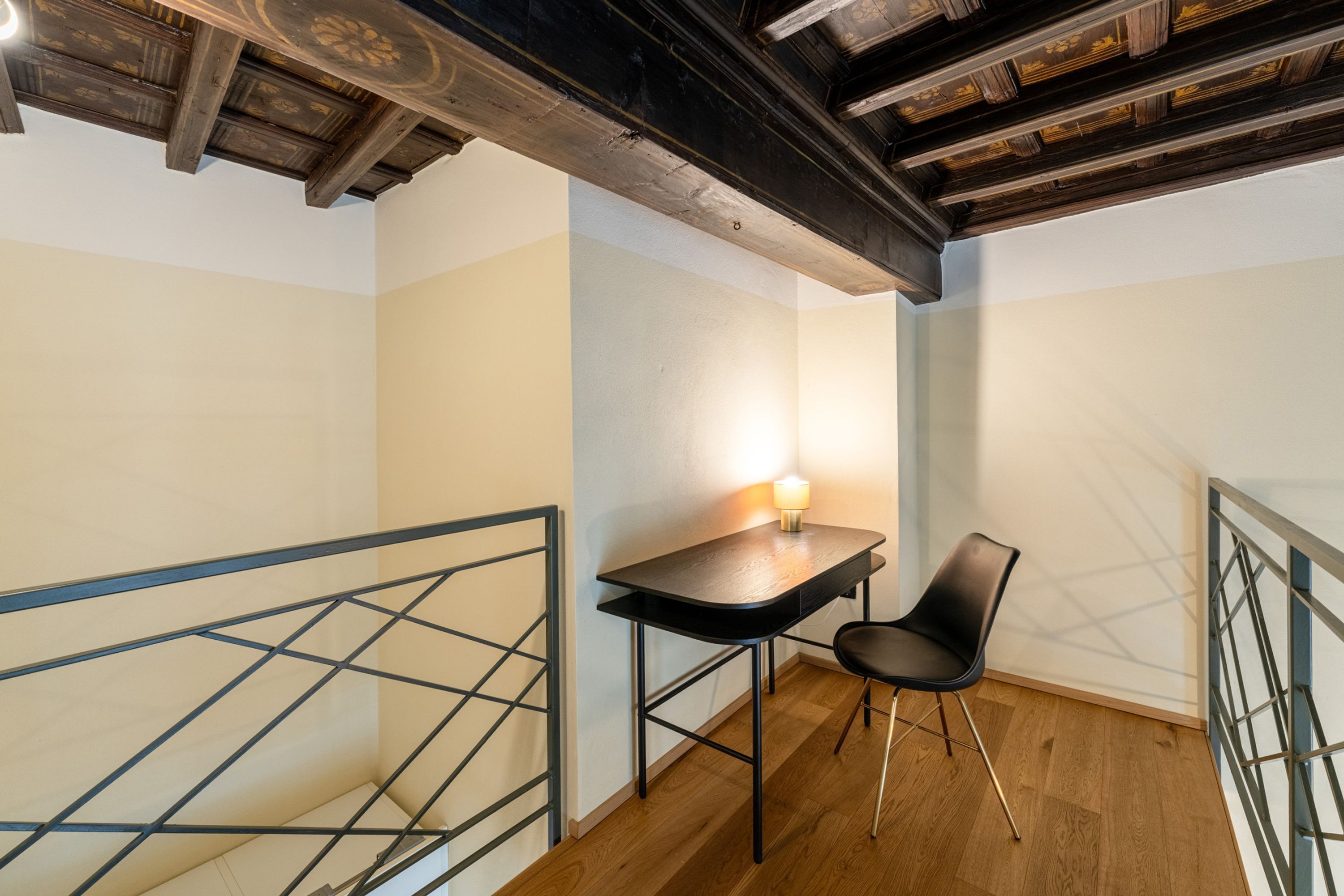 Une petite pièce bien éclairée, avec un plafond en bois, un bureau avec une chaise et une rambarde en métal.