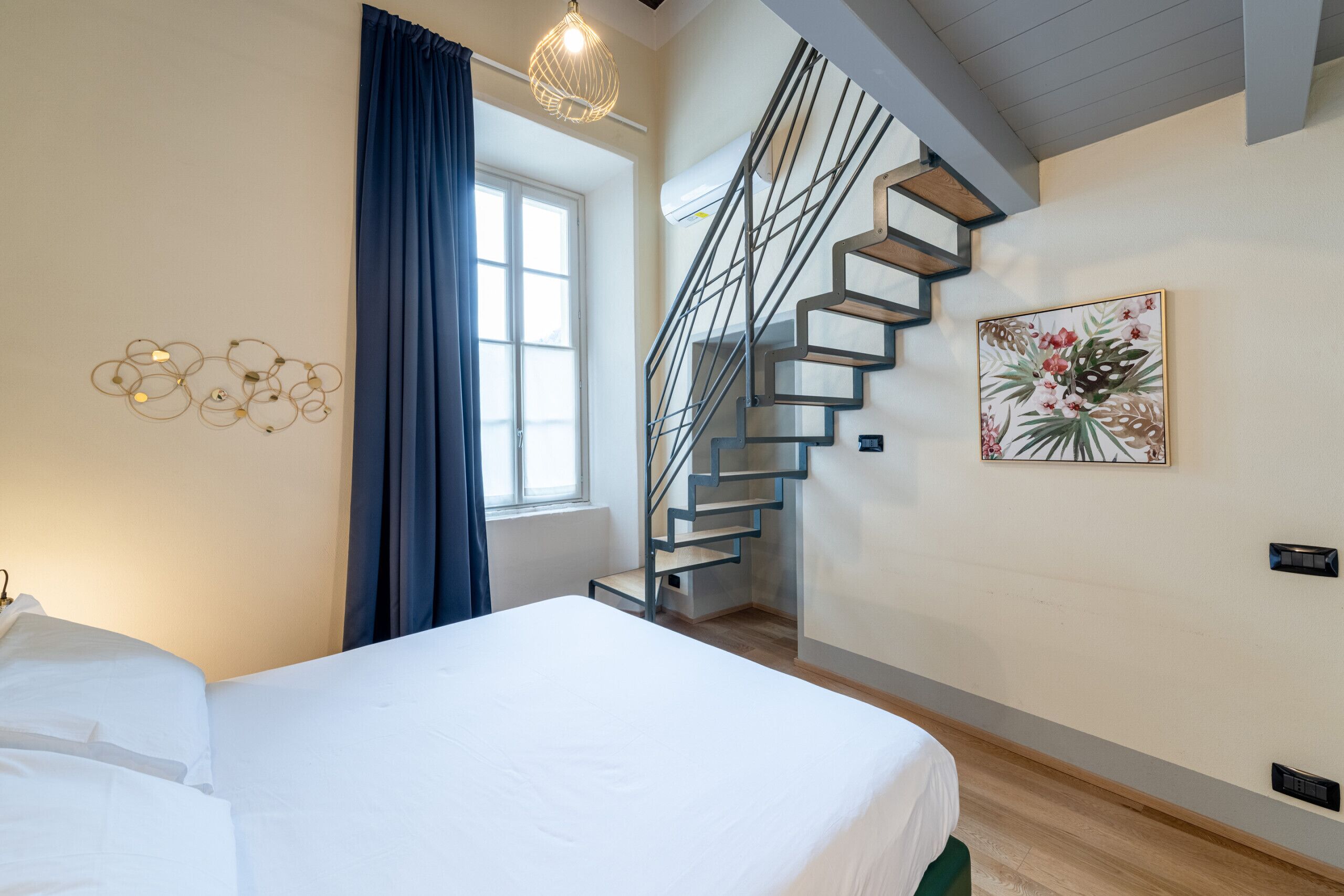 Une chambre moderne avec un lit, un escalier, un luminaire fixé au mur et une œuvre d’art florale.