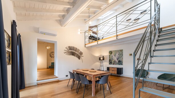 Un vaste espace dédié à la salle à manger, avec une table et des chaises en bois, un escalier et une vue sur un balcon.