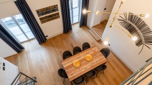 Un espace de salle à manger moderne, avec une table et des chaises en bois, un lustre et une grande fenêtre agrémentée de rideaux.