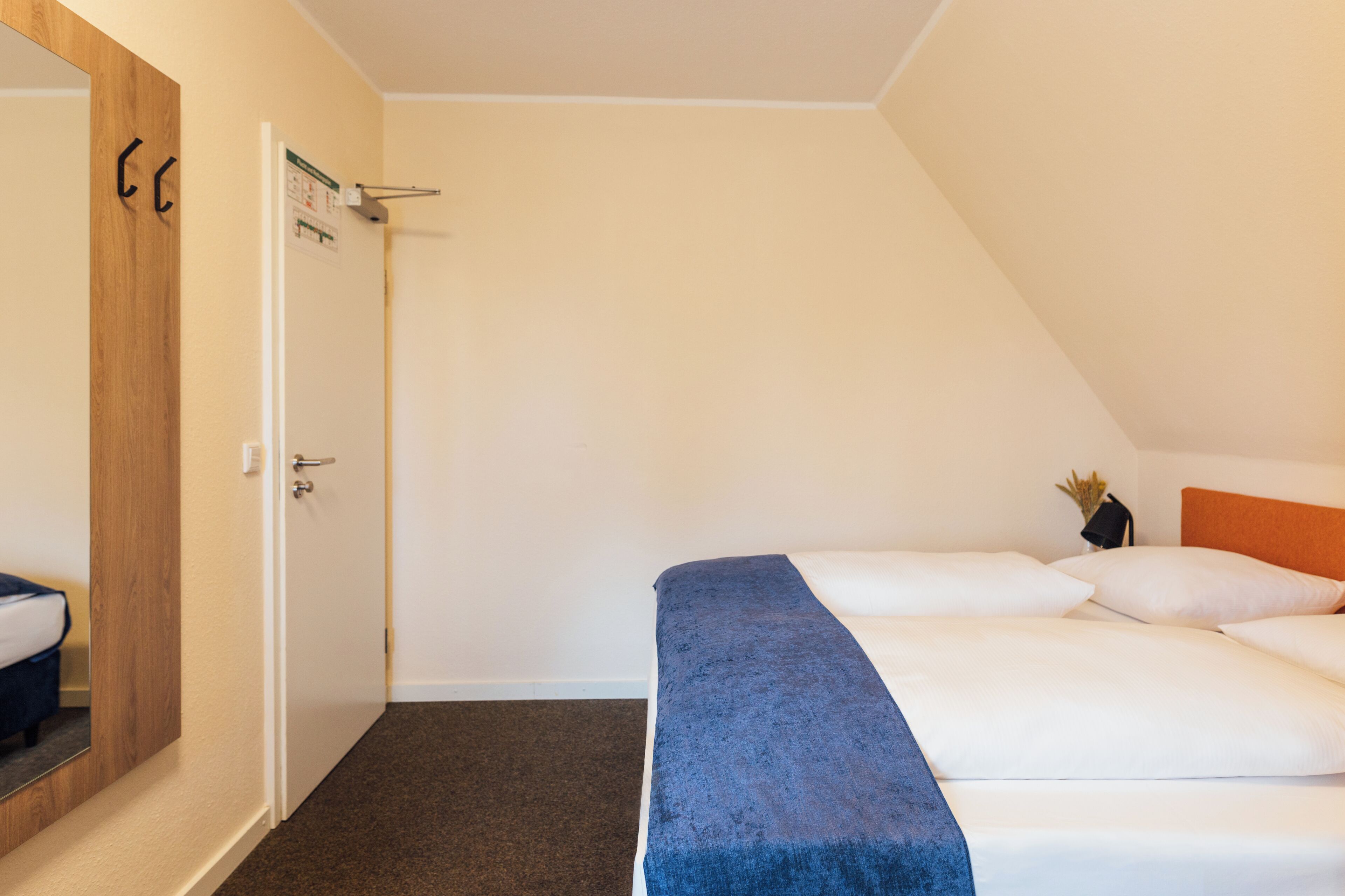 Un dormitorio con cama, puerta de madera, pared blanca y techo inclinado.