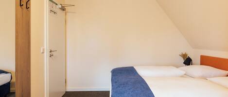 Un dormitorio con cama, puerta de madera, pared blanca y techo inclinado.